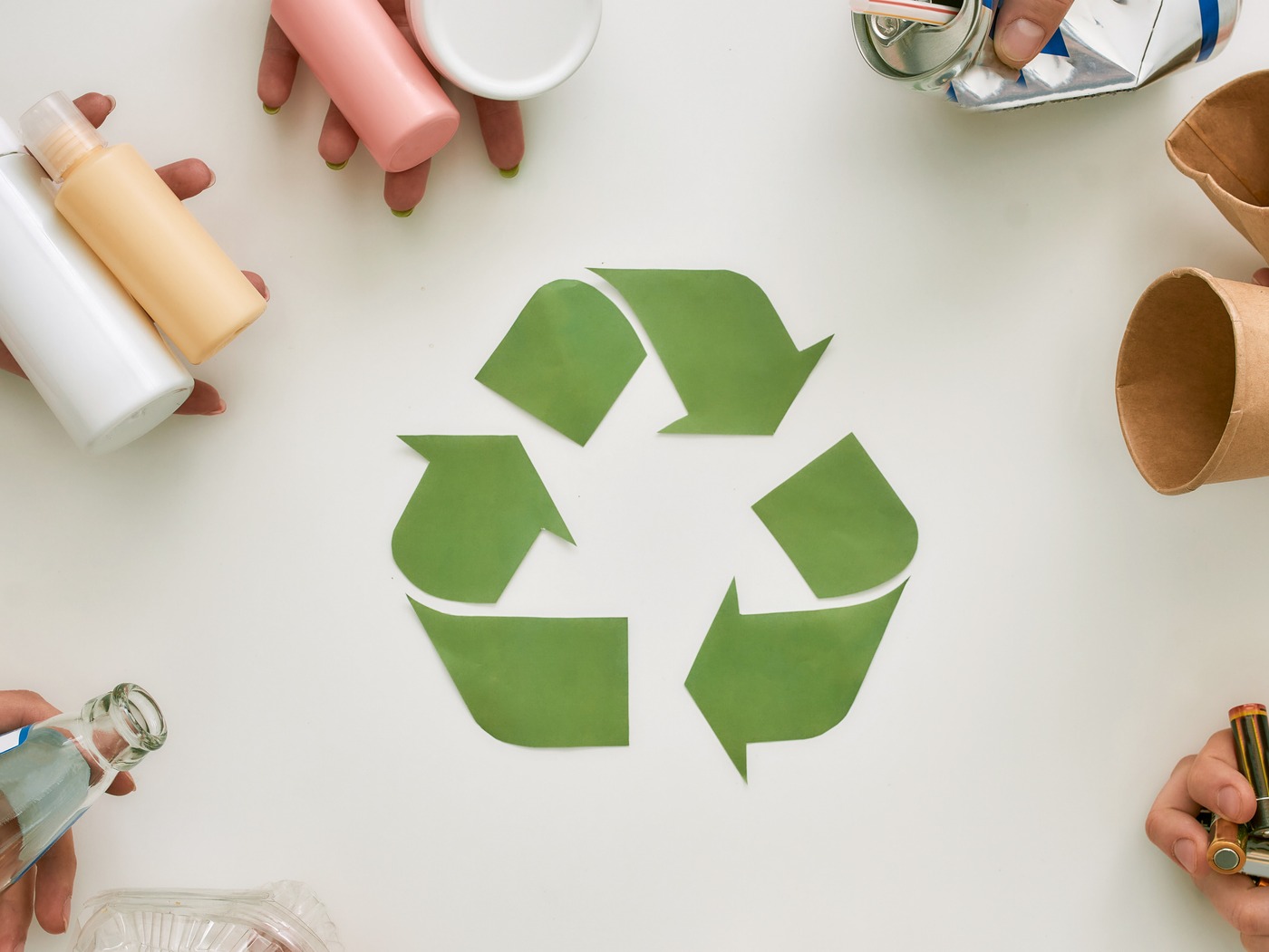 Símbolo del reciclaje en el centro, a su alrededor sujetan distintos residuos