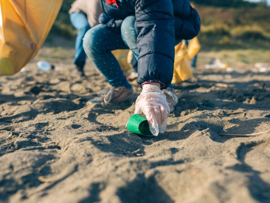 Persona agachada en la arena recogiendo residuos